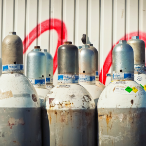 a group of nitrogen gas canisters lined up in front of corrugated iron